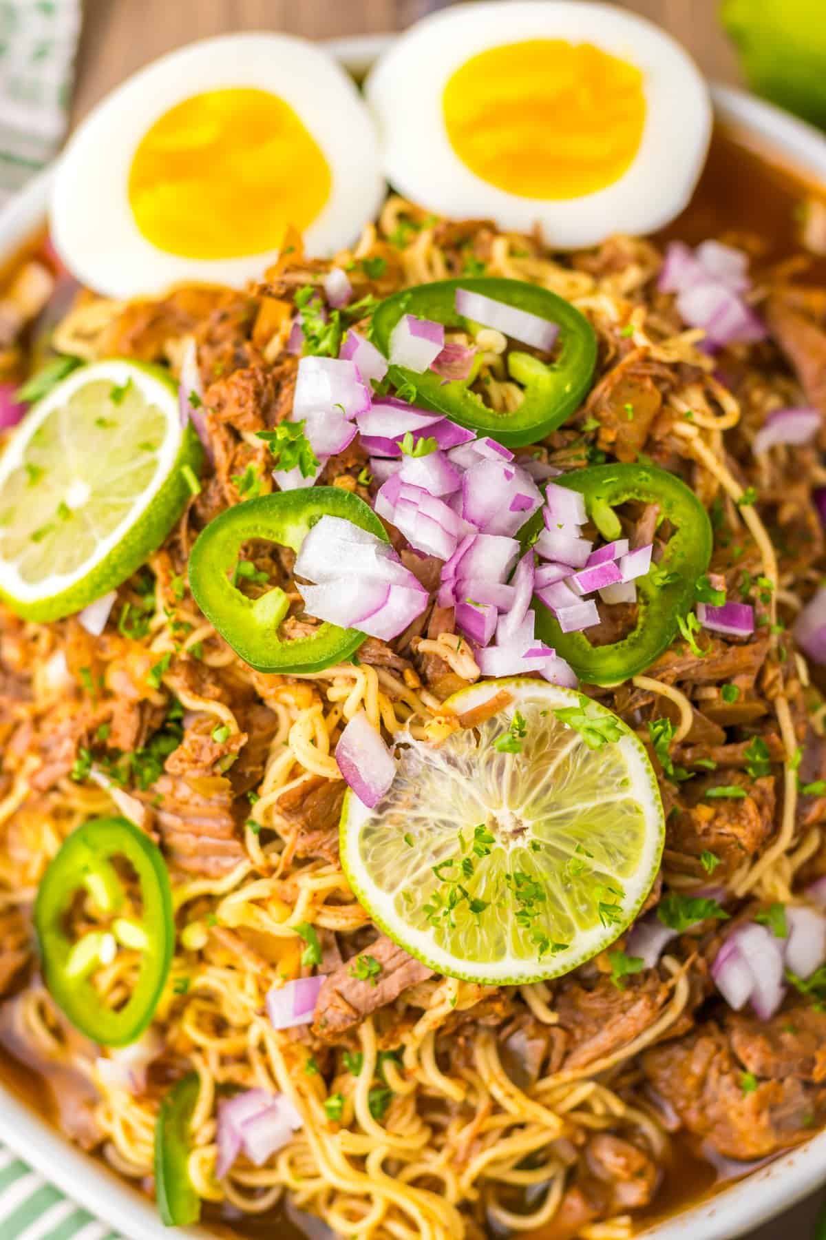 A bowl of birria ramen topped with jalapeno, onion, and lime slices