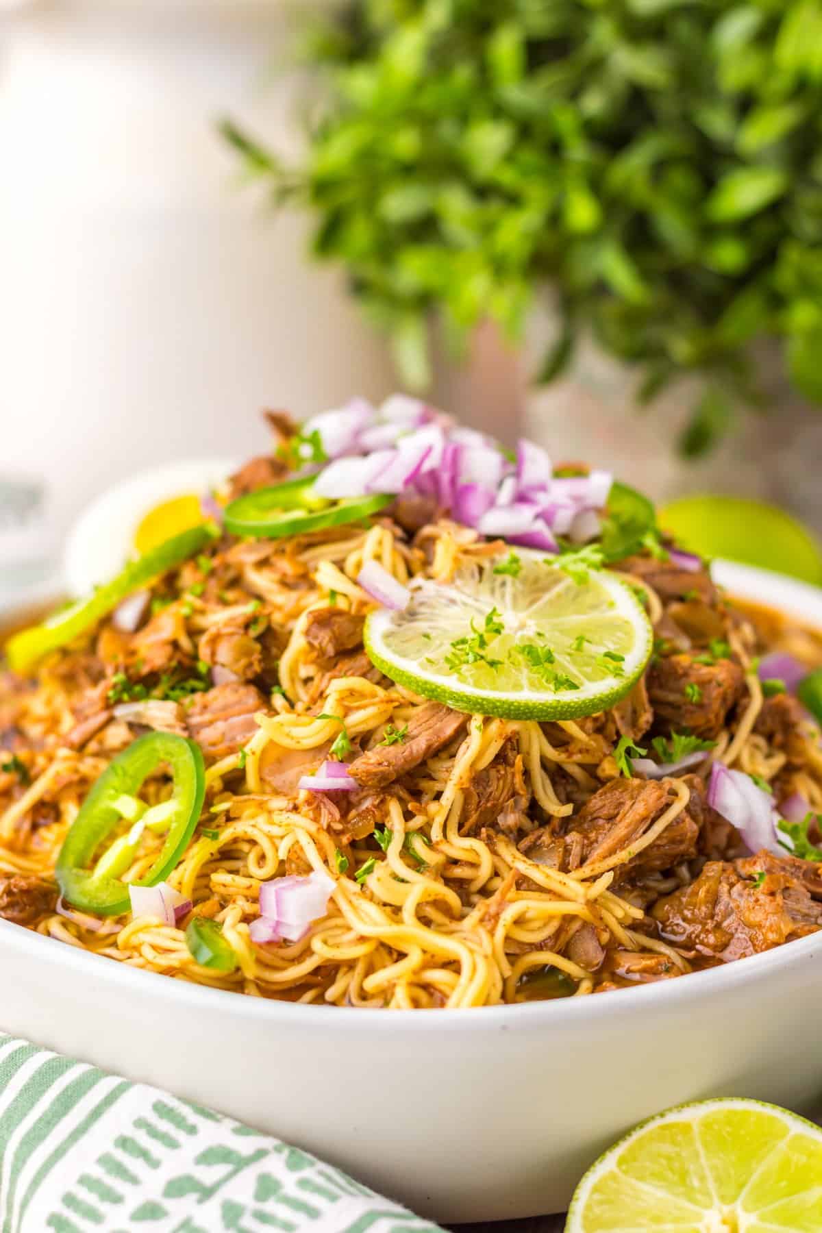 Side view of a bowl of birria ramen with lime and jalapeno slices