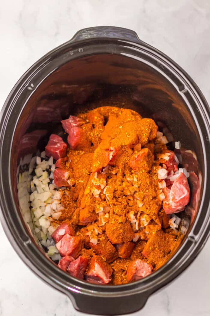 Beef stew meat. onions, garlic, and birria seasoning in a slow cooker