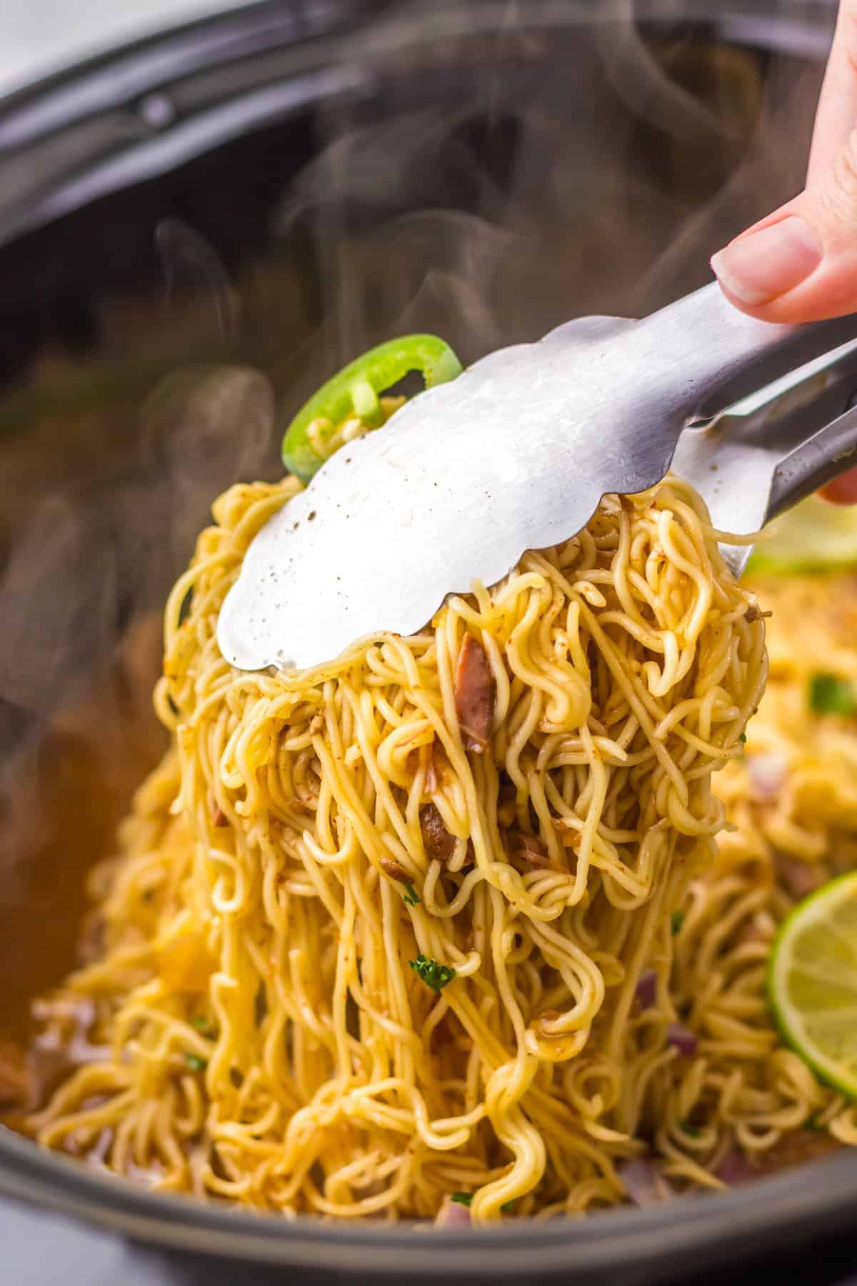 Tongs grabbing birria ramen from the slow cooker