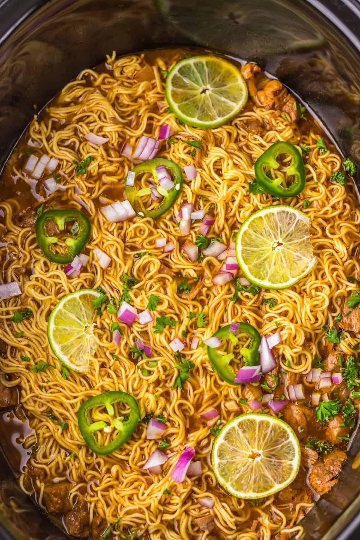 Birria ramen in a slow cooker topped with jalapeno and lime slices