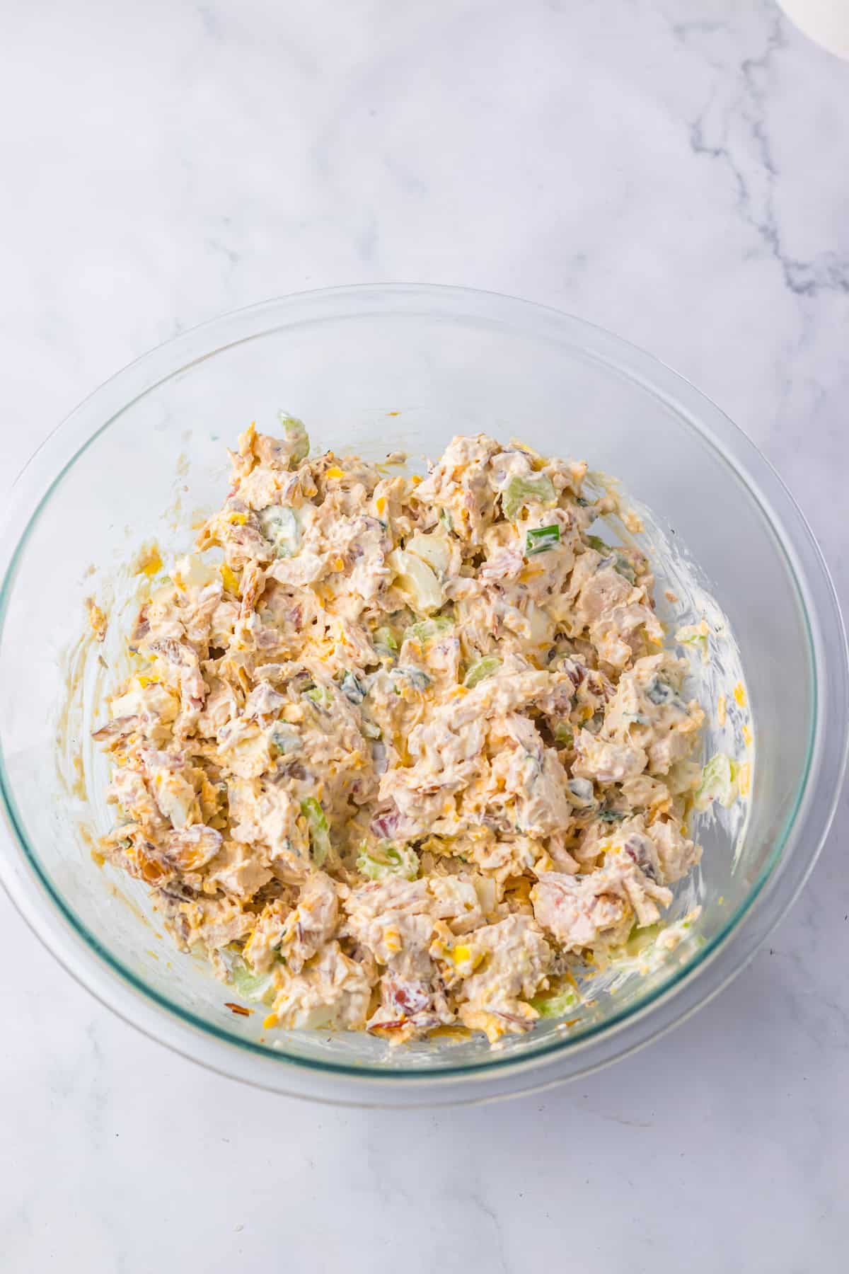 Mixing bowl filled with creamy chicken salad made with bacon, green onions, and almonds, stirred together in a large glass bowl.
