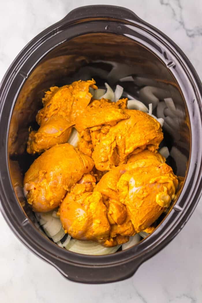 Marinated chicken thighs on top of onion slices in the slow cooker