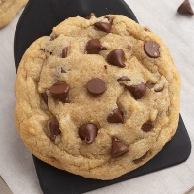 Close up of a spatula lifting a chocolate chip cookie from a lined baking sheet.