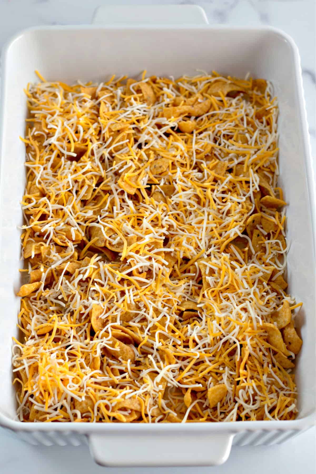 shredded cheese on top of frito chips in a baking dish