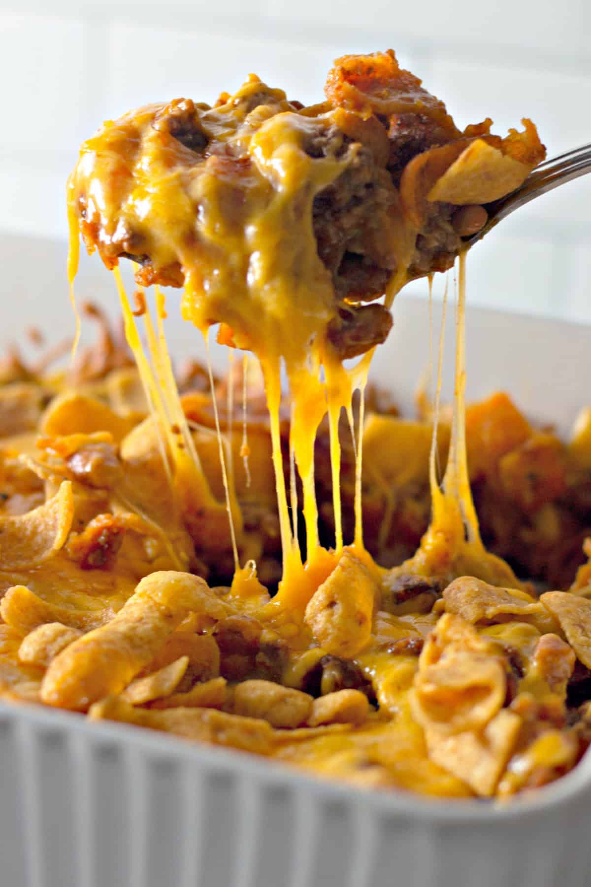 lifting frito pie out of a baking dish with a spoon