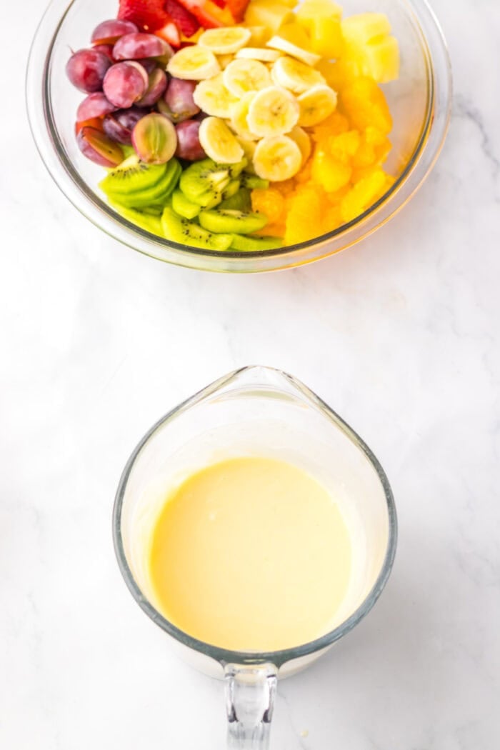 Cheesecake mixture in a measuring cup and a bowl of fruit