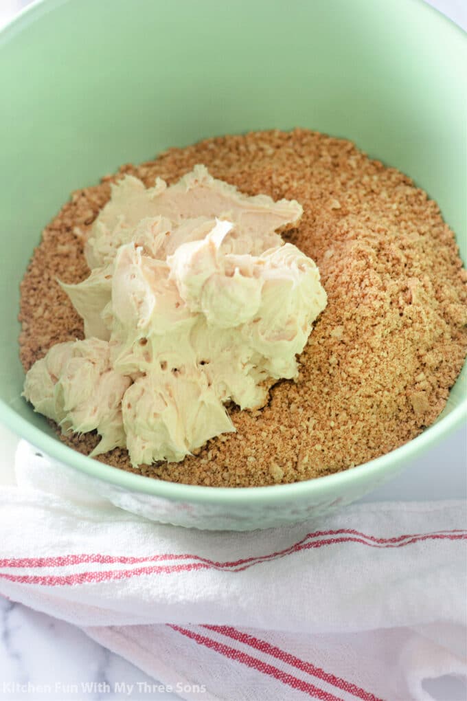 adding the cream cheese, powdered sugar, and peanut butter to the crushed cookies in a mint green bowl.