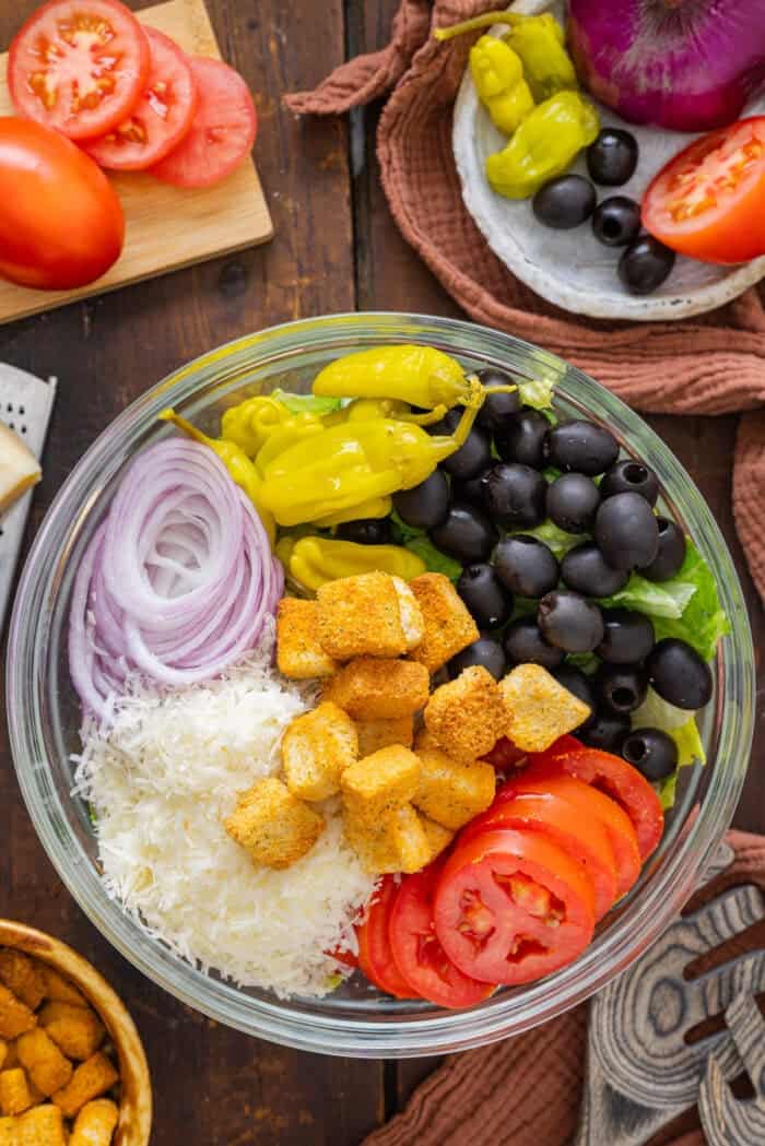 Lettuce, pepperoncini, olives, onion, Parmesan, croutons, and tomatoes in a bowl