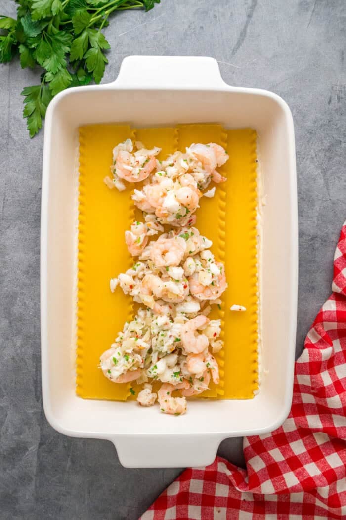 Seafood filling on top of lasagna noodles in a pan