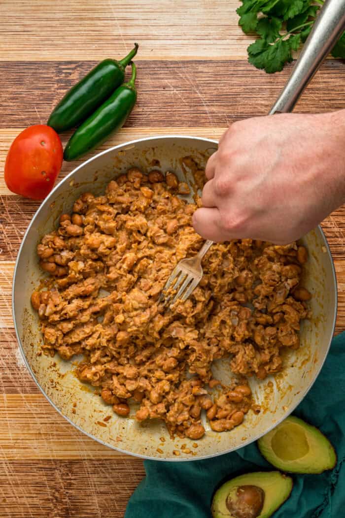 A hand using a fork to mash beans in a pan
